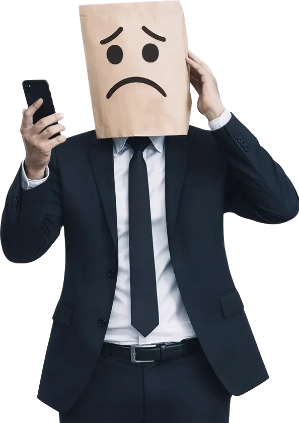 Fotografia de um homem com terno preto completo e gravata, cuja cabeça está totalmente coberta por um saco de papel pardo texturizado com um rosto triste e angustiado desenhado à mão. Ele segura um smartphone preto com a mão direita à frente do peito, e a mão esquerda está levantada em um gesto angustiado ao lado do saco de papel na cabeça. O homem está de pé, isolado contra um fundo preto profundo. A imagem simboliza a tristeza.