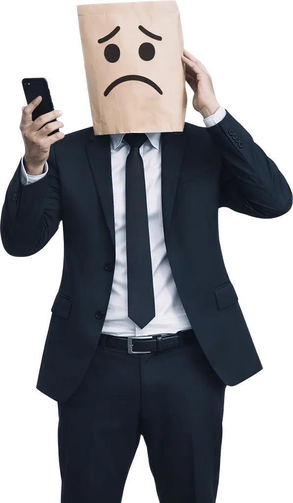 Fotografia de um homem com terno preto completo e gravata, cuja cabeça está totalmente coberta por um saco de papel pardo texturizado com um rosto triste e angustiado desenhado à mão. Ele segura um smartphone preto com a mão direita à frente do peito, e a mão esquerda está levantada em um gesto angustiado ao lado do saco de papel na cabeça. O homem está de pé, isolado contra um fundo preto profundo. A imagem simboliza a tristeza.